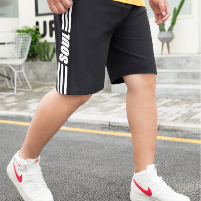 Person wearing black shorts with white stripes and text, white sneakers with red swoosh logo on a street.