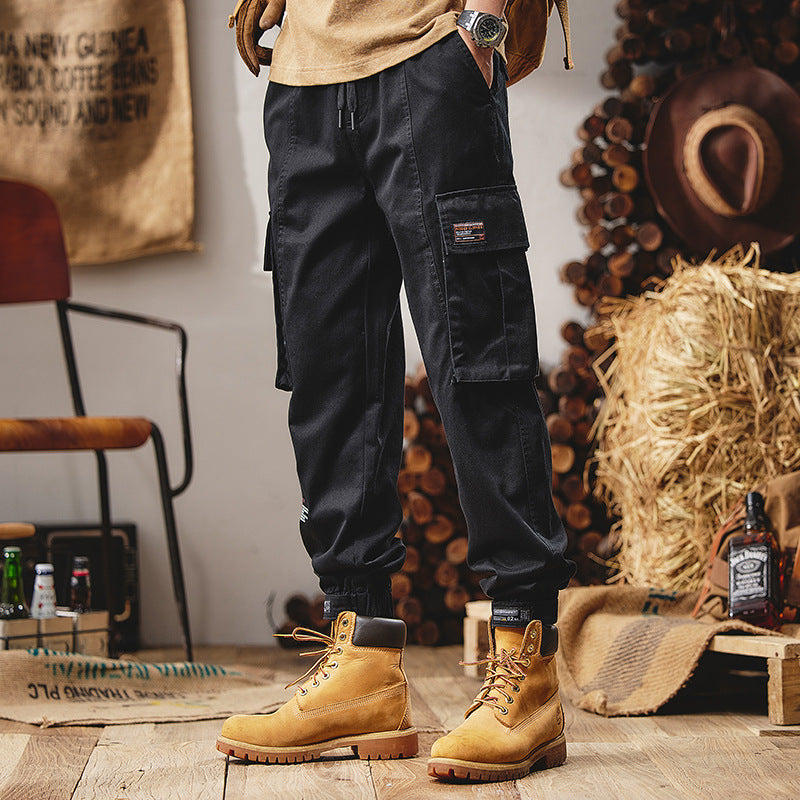 Person wearing black cargo pants and yellow boots in a rustic setting with wood and hay.