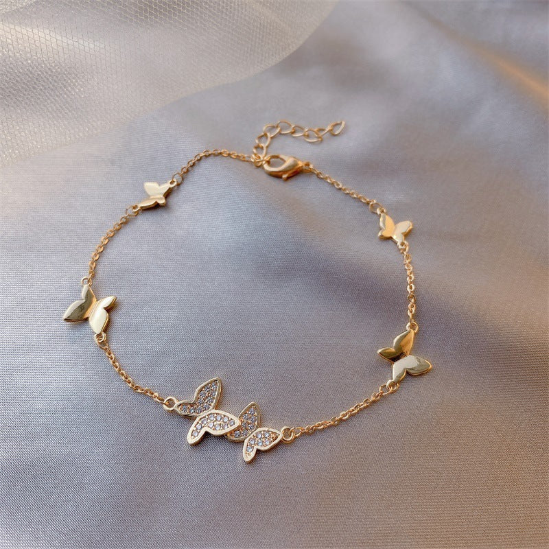 Gold bracelet with butterfly charms on a soft fabric background