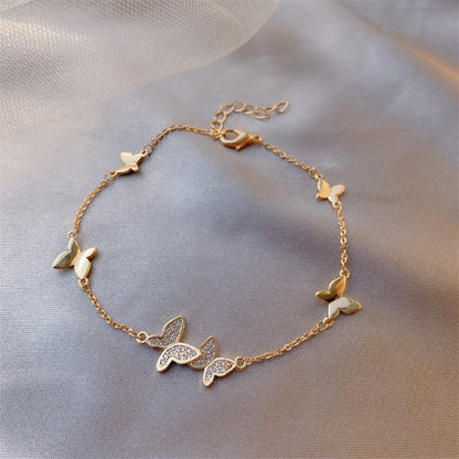 Gold bracelet with butterfly charms on a soft fabric background