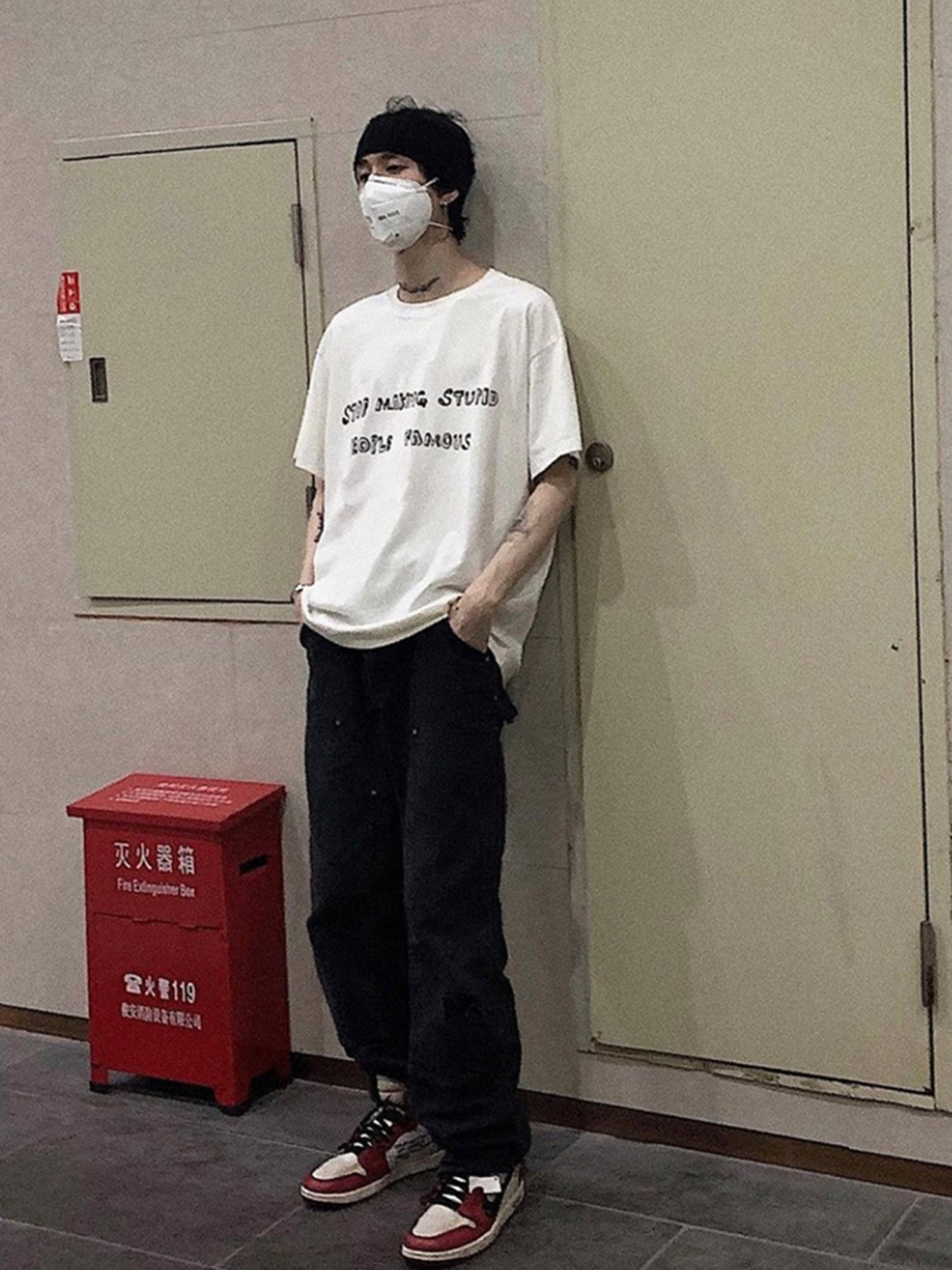 Person wearing a white t-shirt and black pants standing in a room with a red fire extinguisher box.