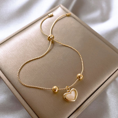 Gold bracelet with a heart charm on a beige box