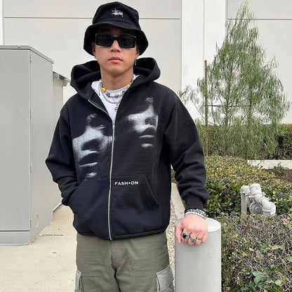 Person wearing a black hoodie with 'FASHION' text, sunglasses, and a hat outdoors.