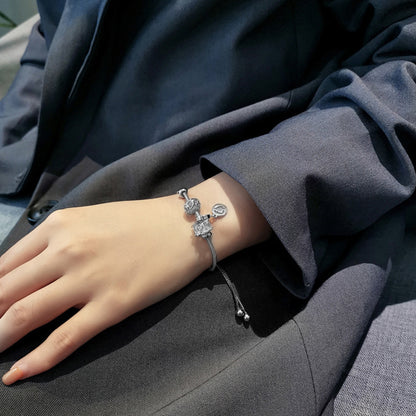 Hand wearing a silver bracelet with intricate designs on a dark fabric background